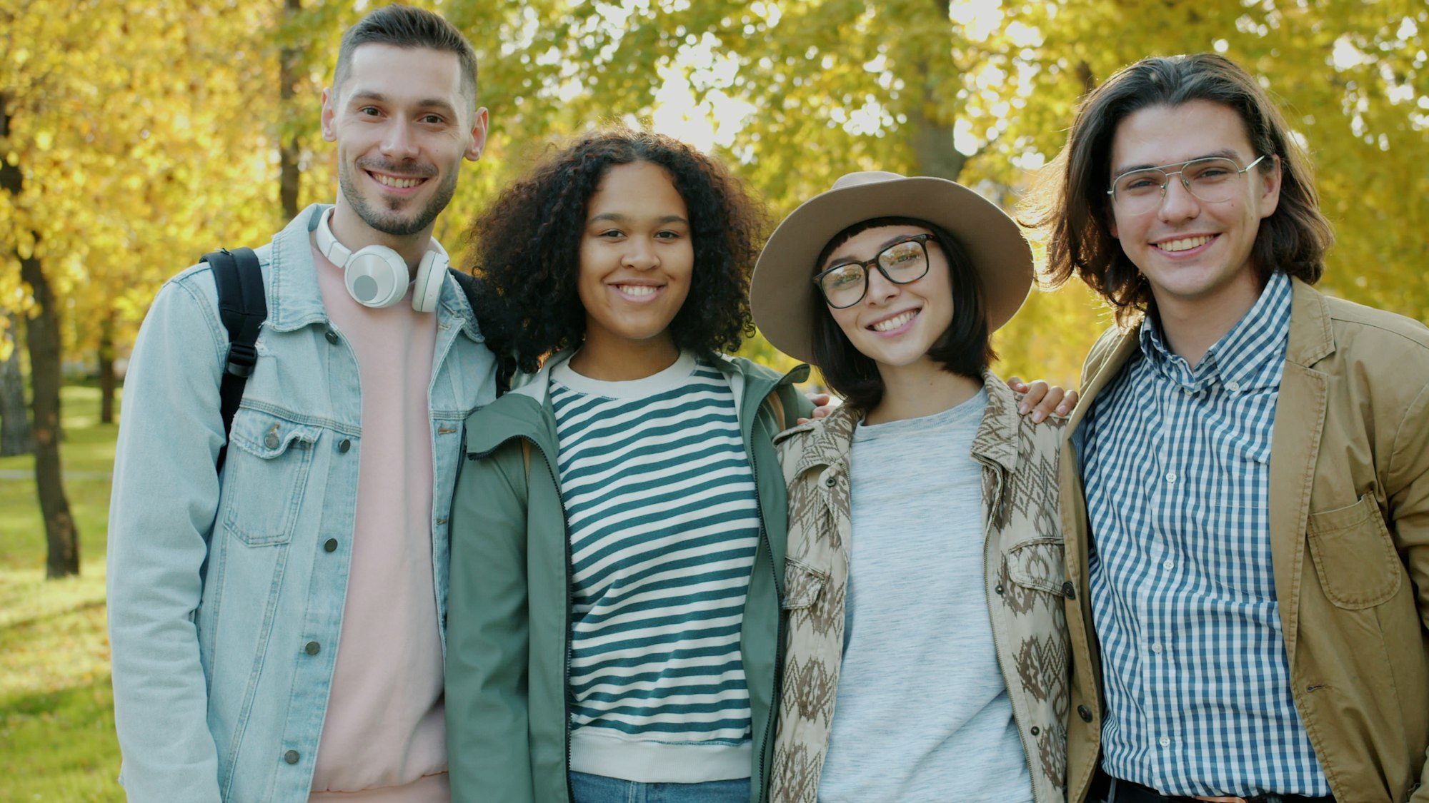 Four young people of different backgrounds standing together outdoors in autumn light